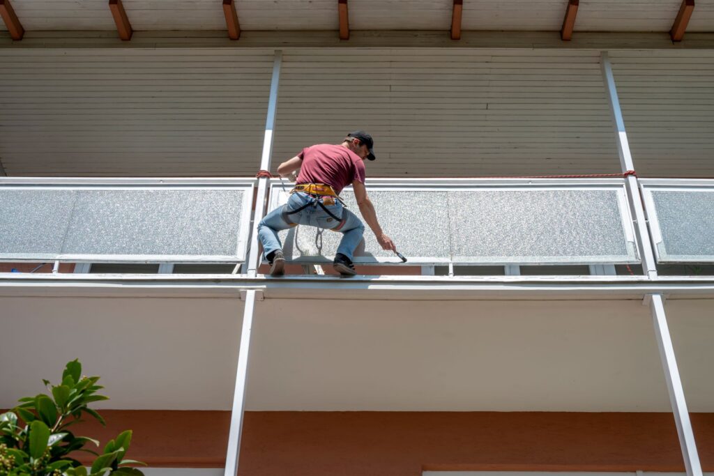 Arbeiter beim Streichen eines Balkons in großer Höhe.