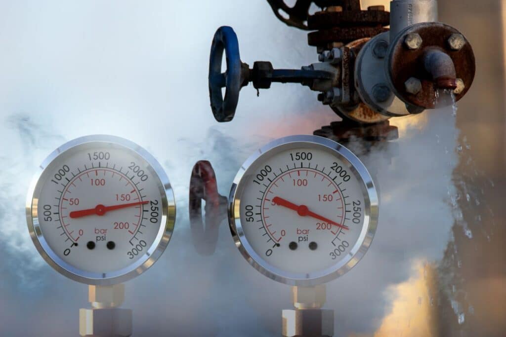 Close-up of two vacuum pressure gauges measuring bar and psi in a steam-filled industrial setting