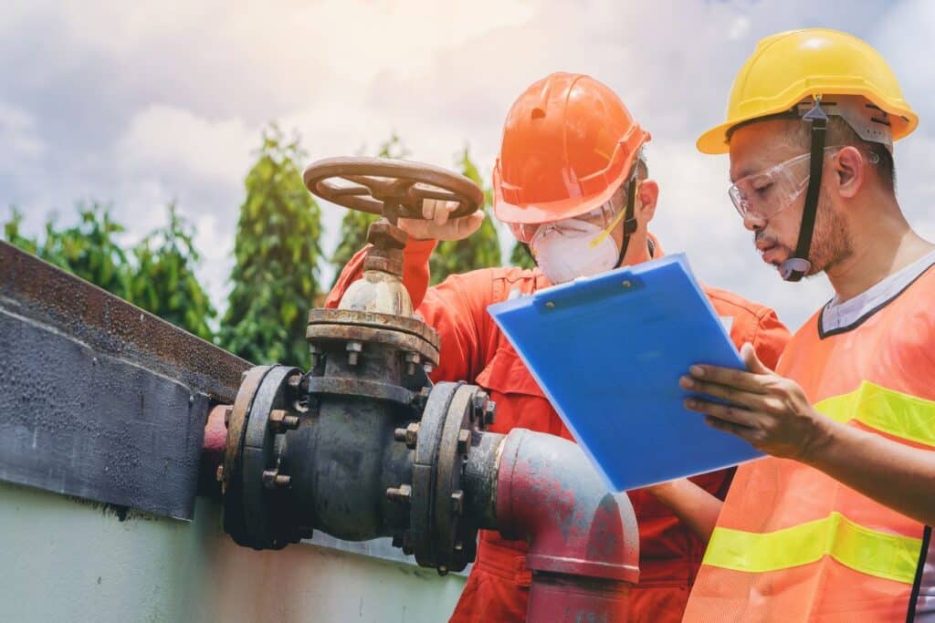 Two technicians in safety gear inspecting a valve with a checklist outdoors