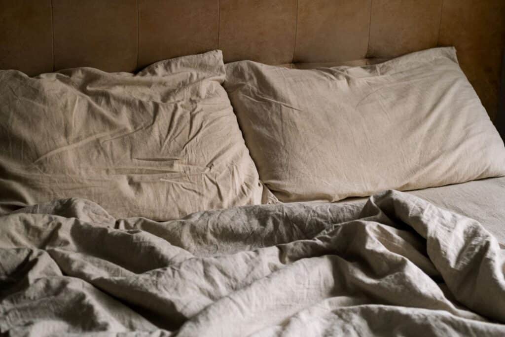 Ungemachtes Bett mit zerknitterter Bettwaesche aus Baumwolle in Naturfarbe – authentischer Look mit Leinenoptik