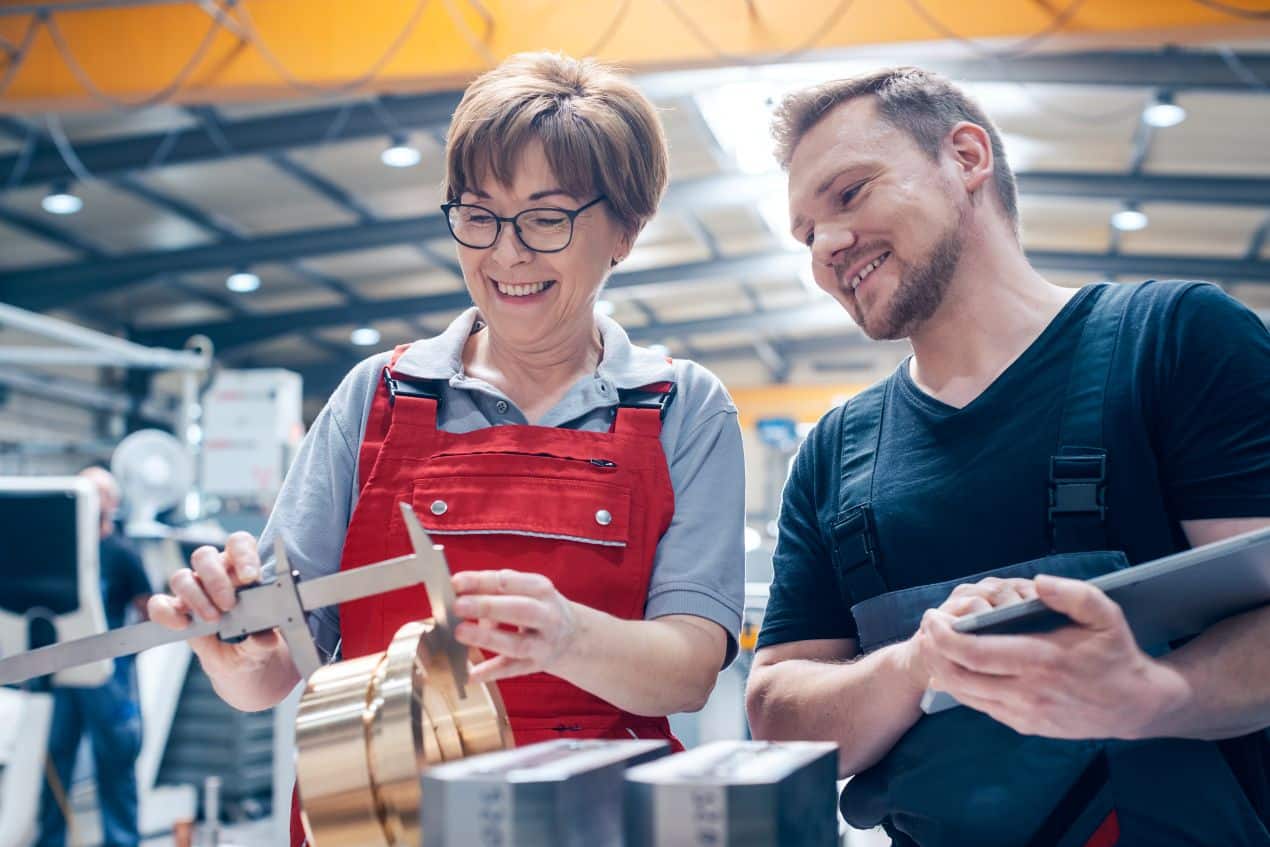 Zwei Fachkraefte pruefen ein Bauteil mit Schieblehre in einer Produktionshalle – Praezision und Zusammenarbeit im Sondermaschinenbau